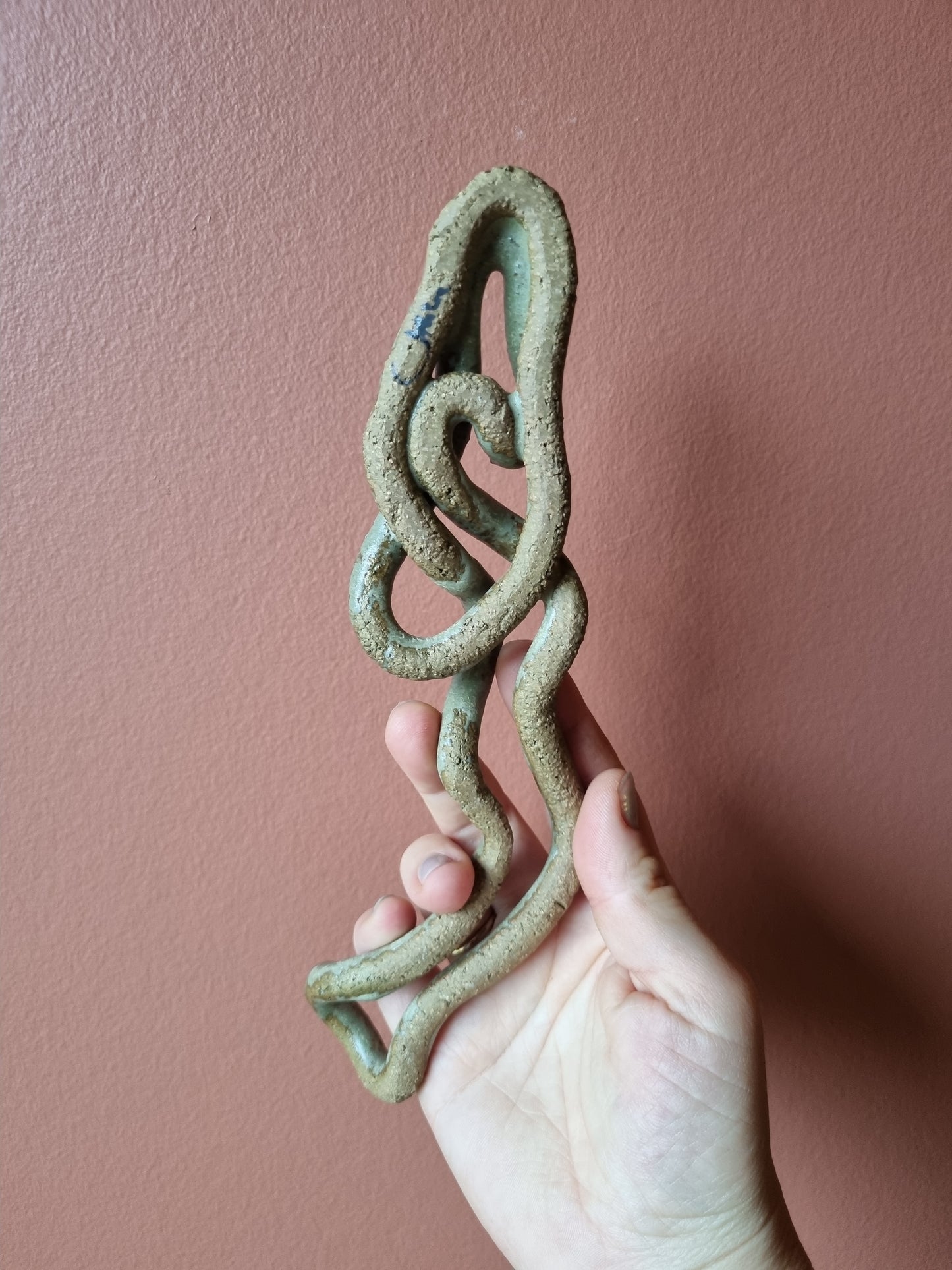 Grønt keramik vægophæng på rosa væg set bagfra